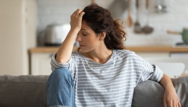 Woman sitting on a couch, appearing stressed and fatigued, representing chronic fatigue and sleep issues related to neck tension and posture, relevant to chiropractic care at Desert Pine Chiropractic in Bellingham, WA.