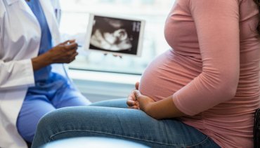 Pregnant woman seated during chiropractic consultation, holding hands on her belly, while a healthcare provider shows an ultrasound image, emphasizing pregnancy care and support at Desert Pine Chiropractic in Bellingham.