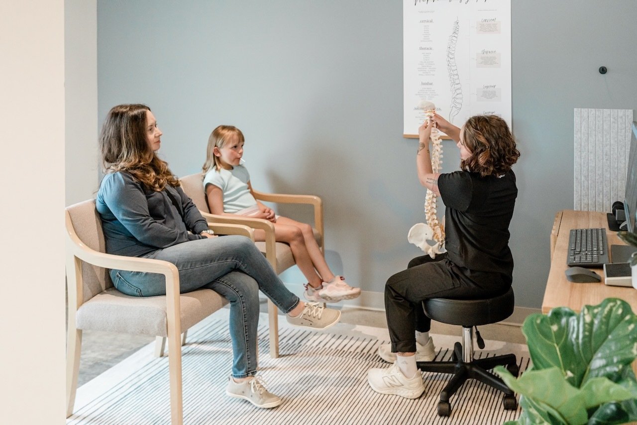 Chiropractor explaining spinal health to a mother and daughter in a welcoming clinic setting, emphasizing personalized care for sciatica and nervous system function.