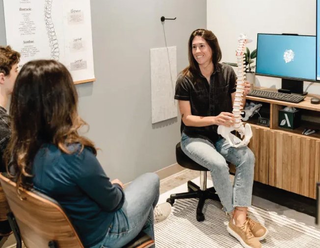 Chiropractor demonstrating spinal anatomy model to patients in a modern clinic setting, emphasizing Torque Release Technique and patient education.