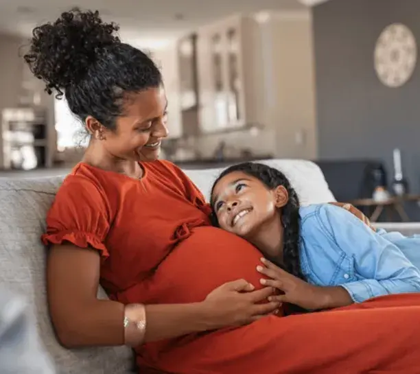 Pregnant woman in red dress smiling at daughter, highlighting prenatal connection and family support during pregnancy.